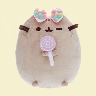 Pusheen is the sweetest cat and this plush soft toy is even sweeter holding a purple lollipop and wearing a colourful rainbow pom pom bow on her head.